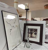 View of framed Ty Wilson Tenderness print, framed Alan Blaustein wine bottles print, Lenox crystal glasses, clear glass decanter, and metal candle holder grouped together