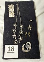 Top-down view of the entire jewelry set laid out on black fabric including bracelet, necklace, three pairs of earrings, and a brooch.
