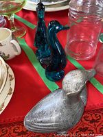 Three bird figurines on a red cloth with dishes and glassware around, showing glass and stone materials.
