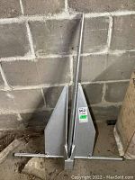 Fortress FX23 boat anchor leaning against a concrete block wall, showing overall shape and size.