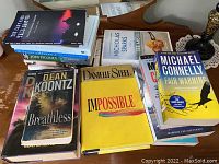 Books stacked and laid out on wooden table showing multiple titles and authors