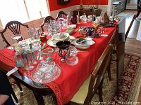 Dining table with red tablecloth and various glass and ceramic items, surrounded by wooden dining chairs with vinyl seats.