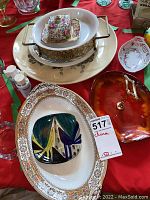 Wide view of multiple serving dishes, including large ornate platter, round bowl on metal stand, smaller floral bowls, salt and pepper shakers, and red decorative plate.