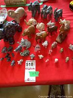 Photo showing multiple elephant figurines of various sizes and materials including wood and glass arranged on a red cloth. Sizes range from small to medium.