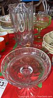 Clear glass pitcher and pedestal serving dishes grouped together on red tablecloth.