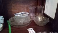 Photo showing the glass bowl, five glass serving plates stacked, and two glass vases grouped together on a shelf