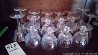 Set of four tall clear glass stemmed glasses with simple design and twelve short stemmed glasses with different styles including etched crystal glasses.