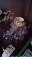 Four stemmed brandy glasses, three smaller stemmed glasses, nine Limoges saucers and one teacup arranged on dark wood shelf
