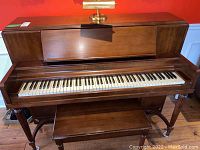 Front view of Heintzman upright piano with bench and piano light on top.