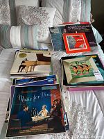 Photo showing a collection of vintage vinyl record albums stacked and laid out on a bed, including albums titled 'Music for Dining' by The Melachrino Strings and several others with mid-century styled covers.