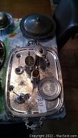 Full view of all items arranged on an ornate silver plated serving tray on a table with floral tablecloth.