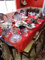 Full view of wood dining table covered with red cloth and various household items for sale.