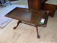Side view of the wood table showcasing the claw feet base and the raised edge around the tabletop with some visible scratches.