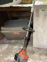Full view of orange and black gas powered weed trimmer with straight shaft and handle, showing overall shape and size.