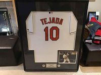 Framed white Orioles jersey with 'Tejada' and number '10' on back, signed by Miguel Tejada on number '1'. Display frame also holds photo and plaque.
