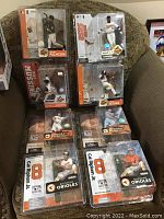 Nine McFarlane Baltimore Orioles figures in unopened packaging displayed on a chair, showing various players.