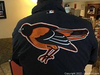 Back view of black parka with large Baltimore Orioles bird logo embroidered in orange and white.
