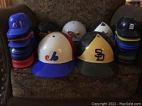 Full-size full face vintage MLB batting helmets and stacks of mini helmets on a chair.