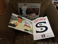 Lot of three baseball themed metal signs lying on a couch; shows the front faces clearly with artwork and text.