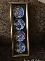 Full front view of framed set of 4 collector plates, vertically mounted in gold-tone frame with black matting. Shows all plates arranged one above the other.