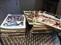Two large stacks of CFL game day programs on a metal table, featuring various teams including Toronto Argonauts and Ottawa Rough Riders, predominantly from the 1970s and 1980s.