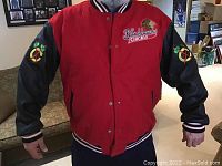 Front view of the Chicago Blackhawks red and black snap button jacket with logo and embroidered text on chest and tomahawks on sleeves.