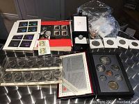 Overview of most lot items laid out on a table showing stamps, coins in cases and ring box