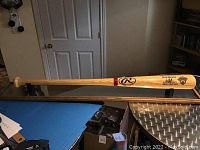 Full view of the natural wood Rawlings Big Stick commemorative baseball bat with Fenway Park inscription resting on black metal stand on table.