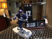 Front view of custom painted Wayne Simmonds figure in Toronto Maple Leafs blue jersey with hockey stick, displayed on round table with original black box behind
