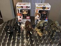 Photograph of all items together: two boxed Funko Pops and five elephant figurines of varying colors and sizes on a table.