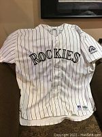 Full front view of white Rockies jersey with 'ROCKIES' lettering and purple pinstripes.