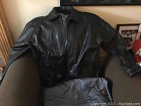 Front view of the black leather jacket displayed on a chair showing zipper closure and snap button cuffs.