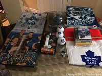 Overall view of the lot showing all 10 Toronto Maple Leafs collectibles on a table, including the clock, Pez dispenser in package, golf balls, Christmas stocking, optical mouse, metal sign, Oyo Sports figure, and ring.
