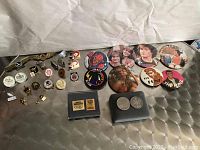 Overview of entertainment and collectible pins and buttons including Farrah Fawcett, Mork & Mindy, The Fonz, Spider-Man, Dick Tracy, and assorted others along with two collectible coins in a plastic case.