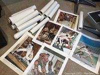 Photo showing several unrolled and rolled up sports prints laid out on the floor, images showing baseball, football, track athletes.
