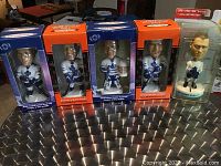 Five Toronto Maple Leafs bobble heads in original packaging displayed on a metal surface, showing front of boxes and one loose figure on right.