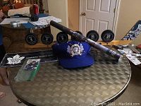 Wood mini stick puck holder with six hockey pucks displaying player jersey numbers and brief write-ups, arranged on a round metallic table along with a blue Maple Leafs starter cap.