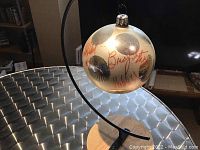 Front view of the silver Christmas ornament showing red autographs of AC/DC band members and reflective silver polka dots, hanging on black metal wire attached to wooden base.