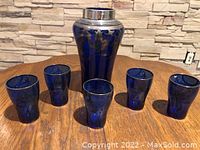 Photo showing blue cobalt glass vase with silver designs and metal top, surrounded by five matching blue glass drinking glasses with silver accents.