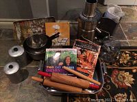 Photo showing multiple kitchen items: stainless steel mixing bowls, cookbooks, metal canisters, wooden rolling pins, a ladle, and metal spatula on a baking sheet.