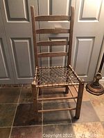 Front view of the wooden chair showing the ladder-back and woven rope seat on tiled floor.