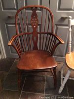Wooden chair with carved spindle back, armrests, and contoured seat, medium brown finish.