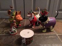 Photo showing five Fitz and Floyd ceramic Christmas animal figurines: a deer with rider, two dogs dressed in holiday attire including soldier and purple outfit with wreath, and a small cylindrical container.