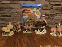 Full set of five David Winter collectible cottages arranged on a wooden table in front of the original box showcasing the range of cottage styles and sizes.