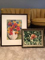 Two framed floral artworks placed side by side. Larger one is a colorful flower painting in a dark wood frame, smaller one is a pink rose photo in a metallic frame.