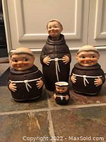 All four Goebel monk figurines grouped showing size variation and facial expressions on tiled floor.