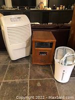 Three appliances on floor: white Whirlpool Plus appliance on left, wooden heater in center, white humidifier or air filter on right with cord coiled on top.