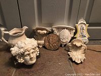 Photo of six decorative pieces including a ceramic planter bust, wall plaques, and a clock motif piece.