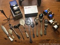 Full overview of lot items including opera glasses in box, metal utensils, and wind chime parts on table