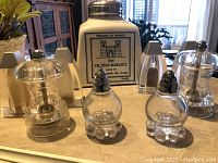 Multiple salt and pepper shakers on a table with natural light, showing the variety of materials and shapes.
